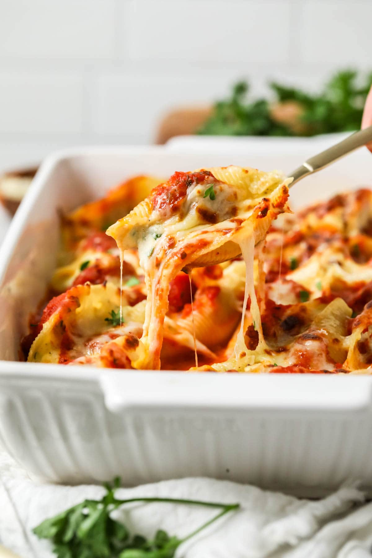 Spoon lifting a serving from a pan of stuffed shells.