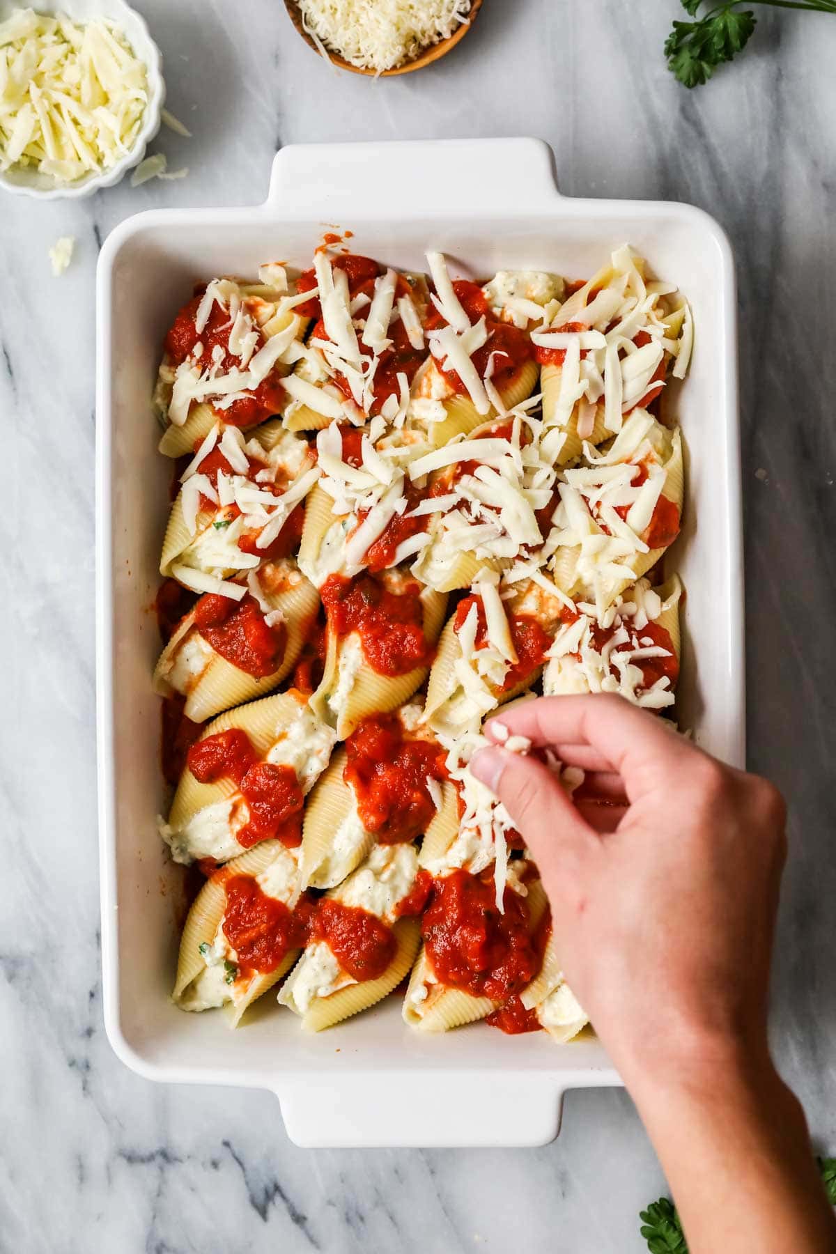 Overhead view of jumbo pasta shells being topped with sauce and shredded cheese.