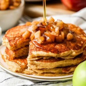 Close up of apple pancakes on a plate, syrup being poured overtop