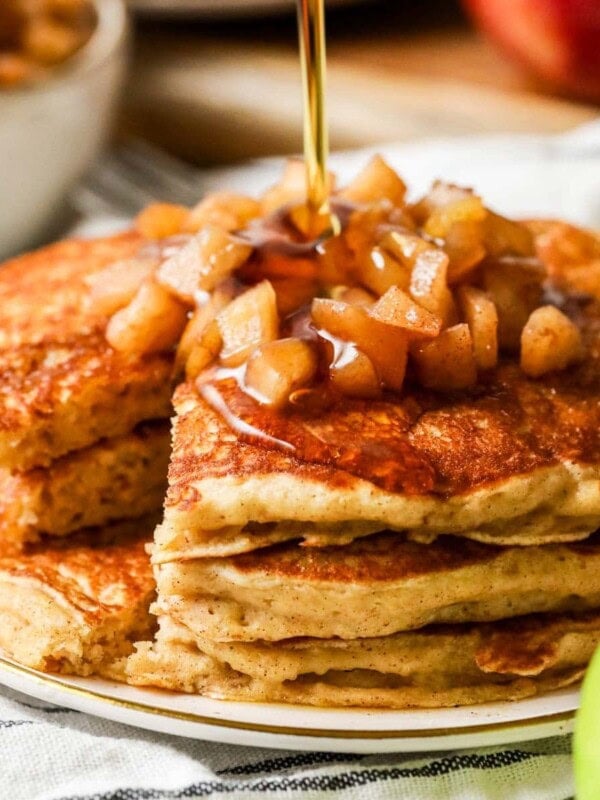 Close up of apple pancakes on a plate, syrup being poured overtop