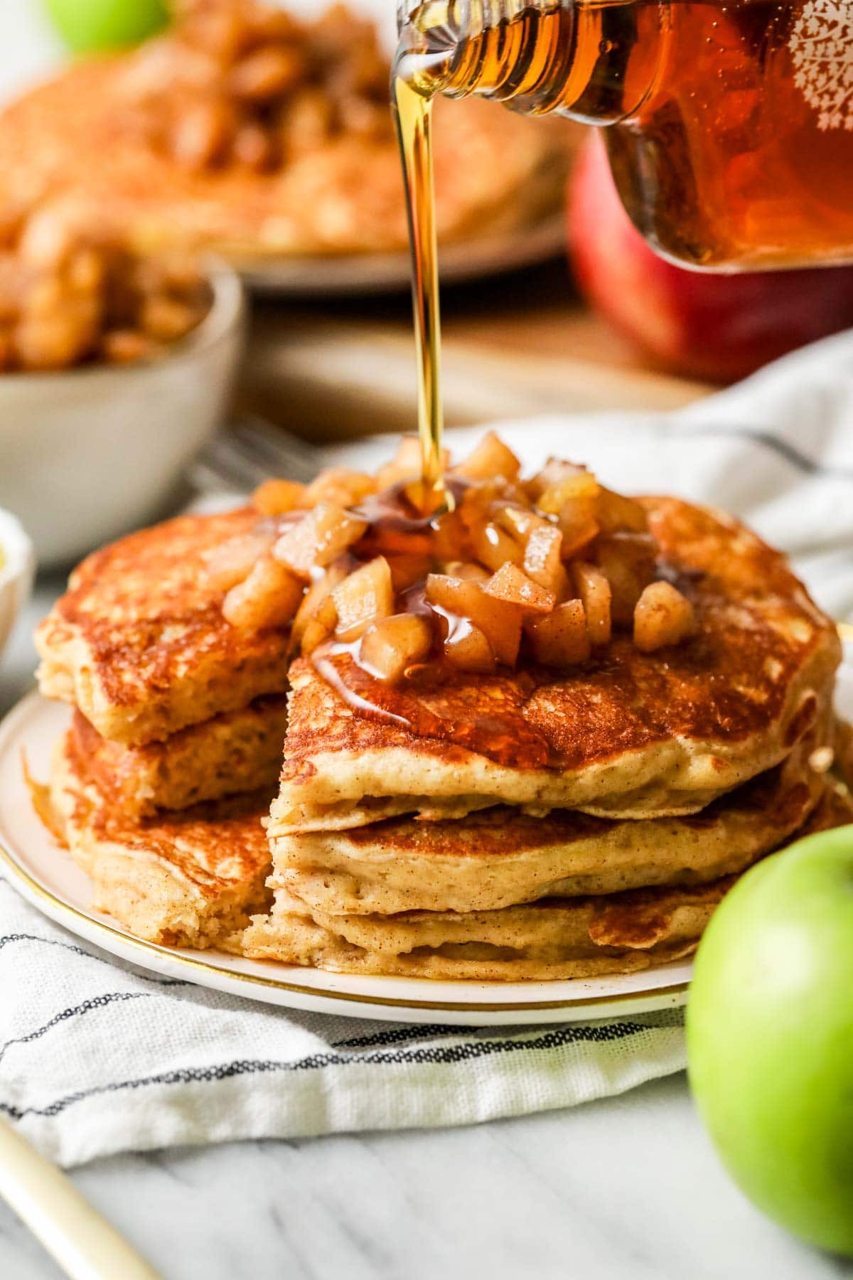 pouring syrup on a stack of apple pancakes