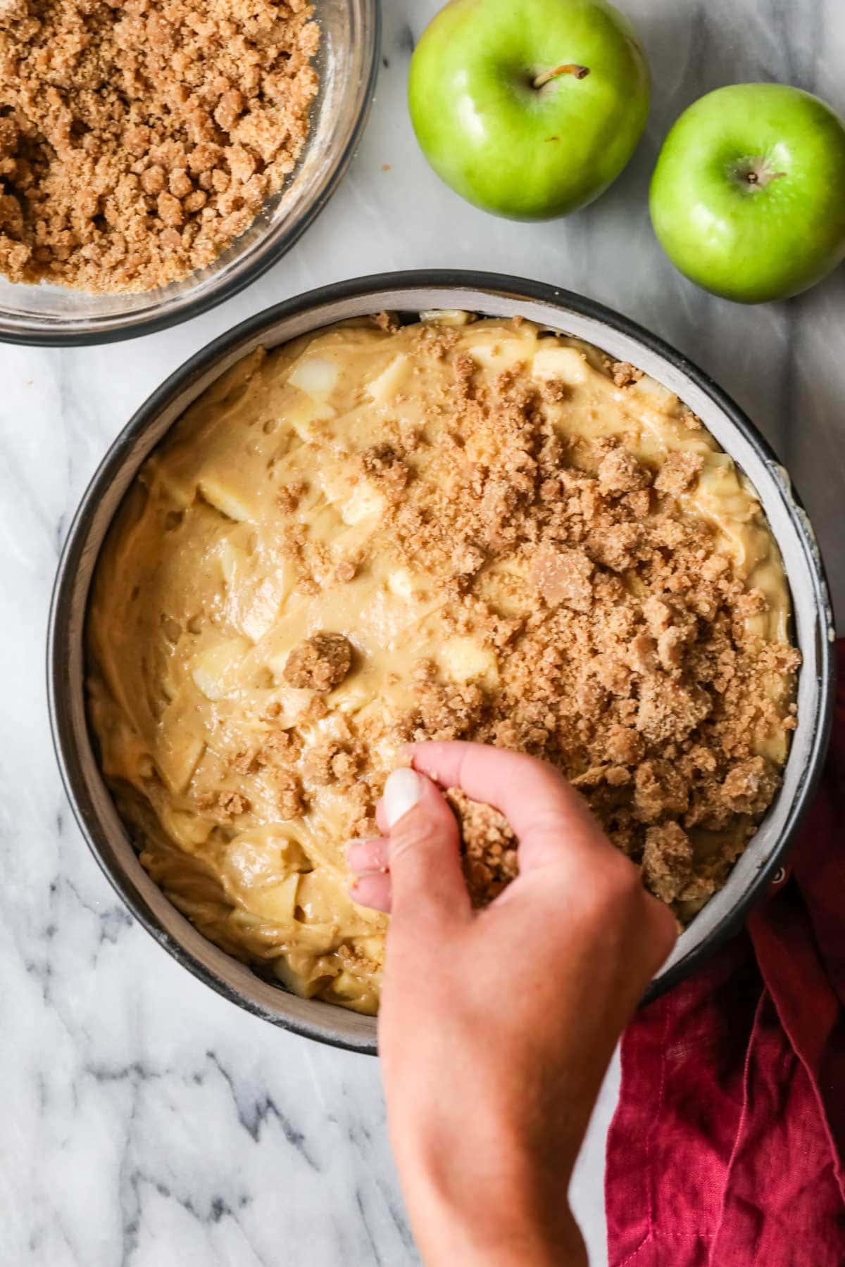 Sprinkling streusel over apple crumb cake batter in springform pan