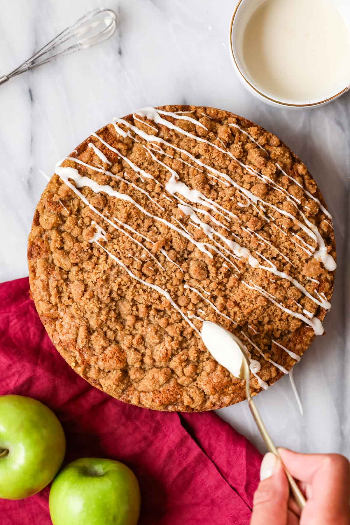 Overhead of an apple cake in springform pan being drizzled with vanilla glaze