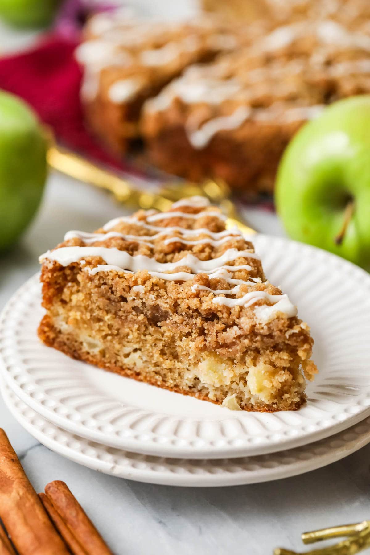 Slice of apple crumb cake drizled with vanilla glaze on a white plate