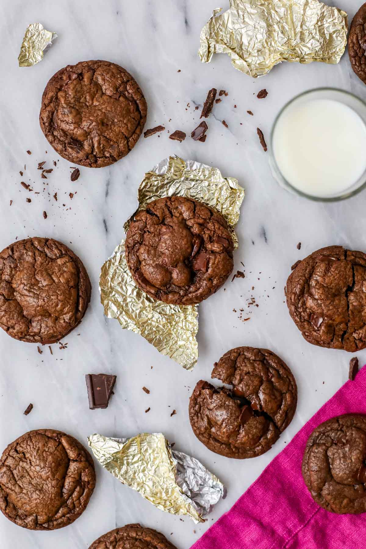 Overhead view of a chocolate cookie in a gold foil wrapper surrounded by other cookies and chocolate shards.