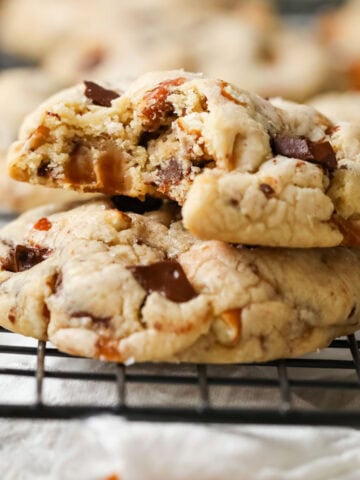 Two pretzel caramel chocolate cookies stacked on top of each other with the top cookie missing a bite.