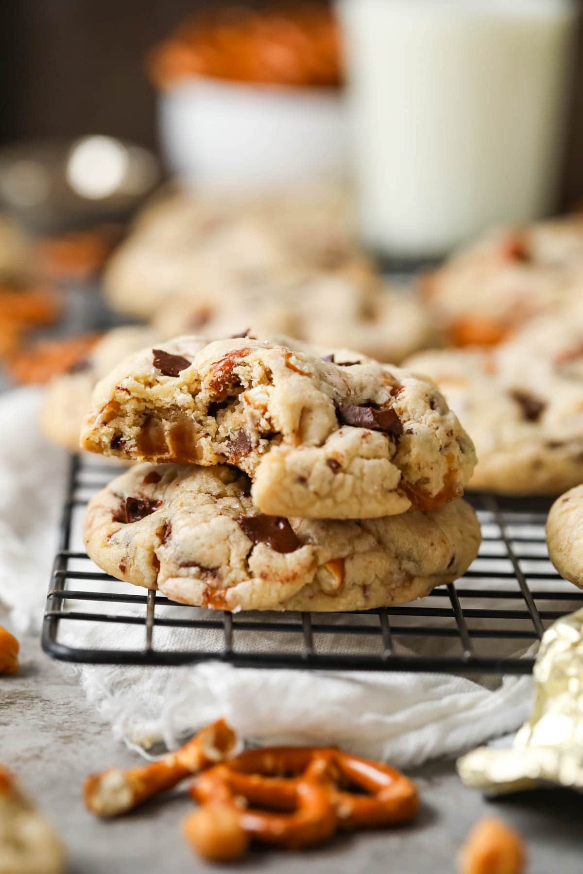 Two pretzel caramel chocolate cookies stacked on top of each other with the top cookie missing a bite.