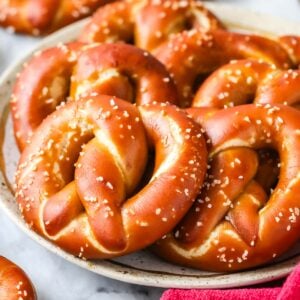 Pile of deep golden brown sourdough soft pretzels on a plate.