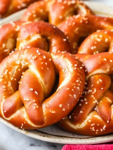 Pile of deep golden brown sourdough soft pretzels on a plate.