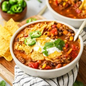 Bowl of taco soup topped with corn chips, jalapeno, sour cream, and more.