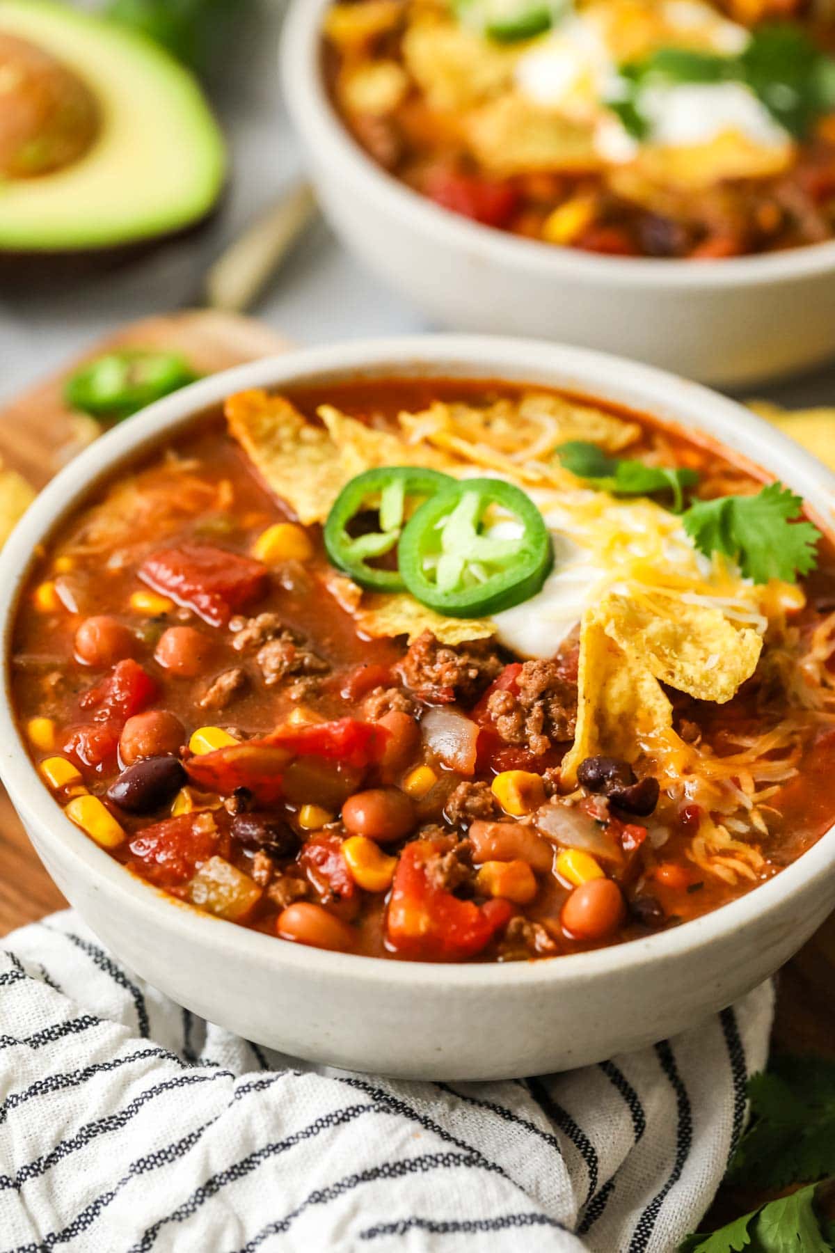 Close-up view of a bowl of soup topped with jalapeno, corn chips, and sour cream.