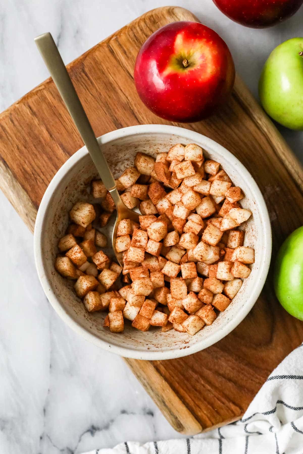 apple pieces in a white bowl tossed with cinnamon and sugar