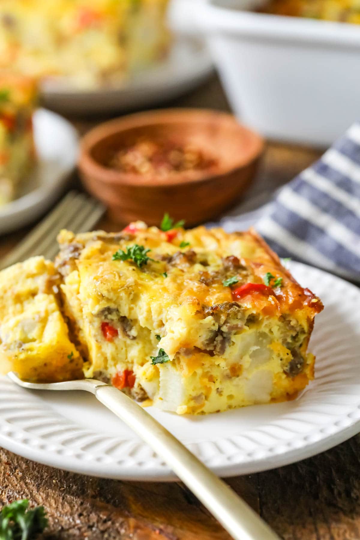 Fork taking a bite from a slice of casserole made with eggs, sausage, peppers, and more.