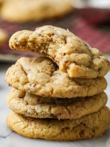 Stack of brown butter toffee cookies with the top cookie missing a bite.