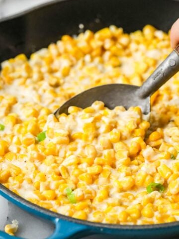 Spoon scooping creamed corn out of a skillet.