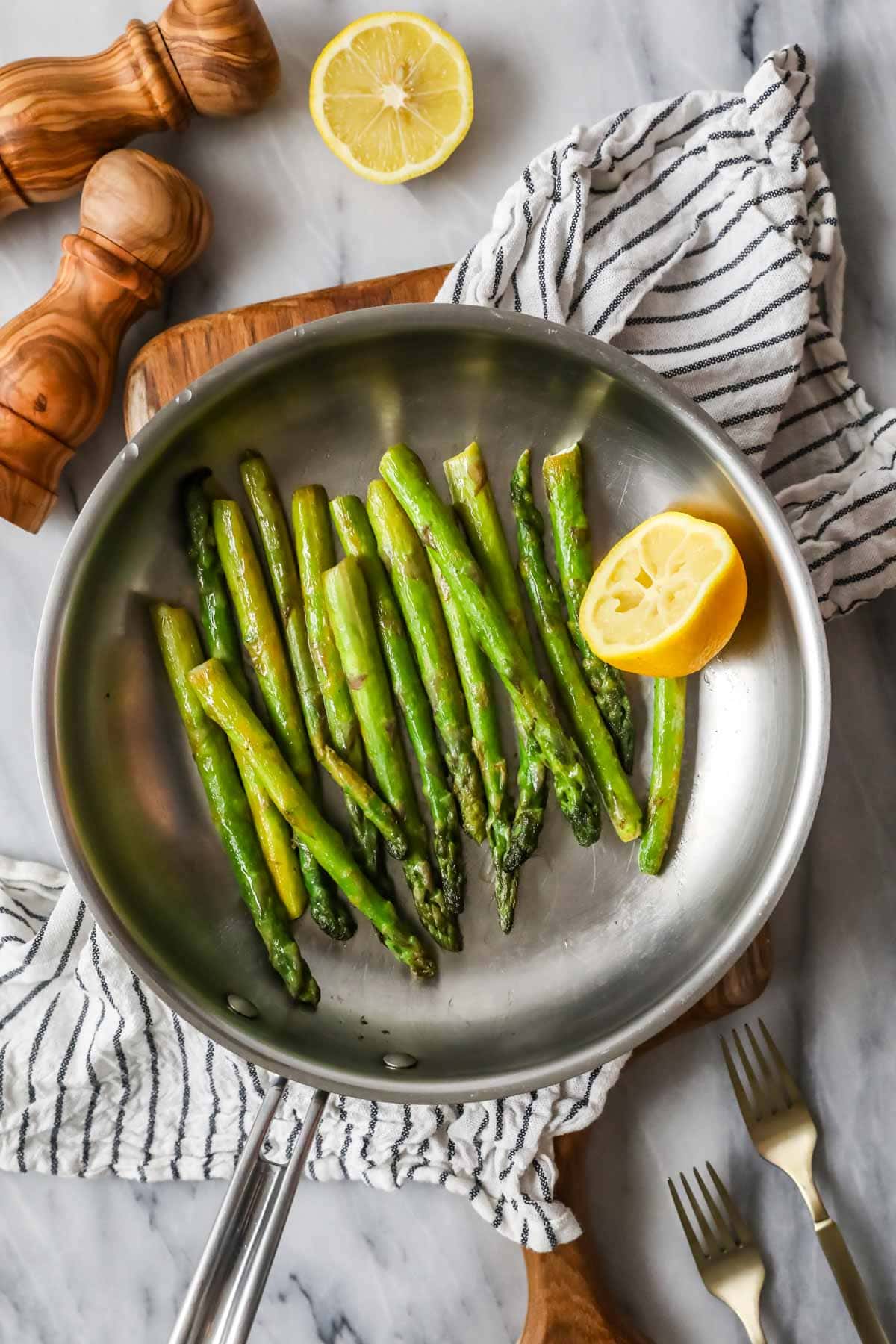 Overhead view of sautéed asparagus in a saucepan with a lemon half.