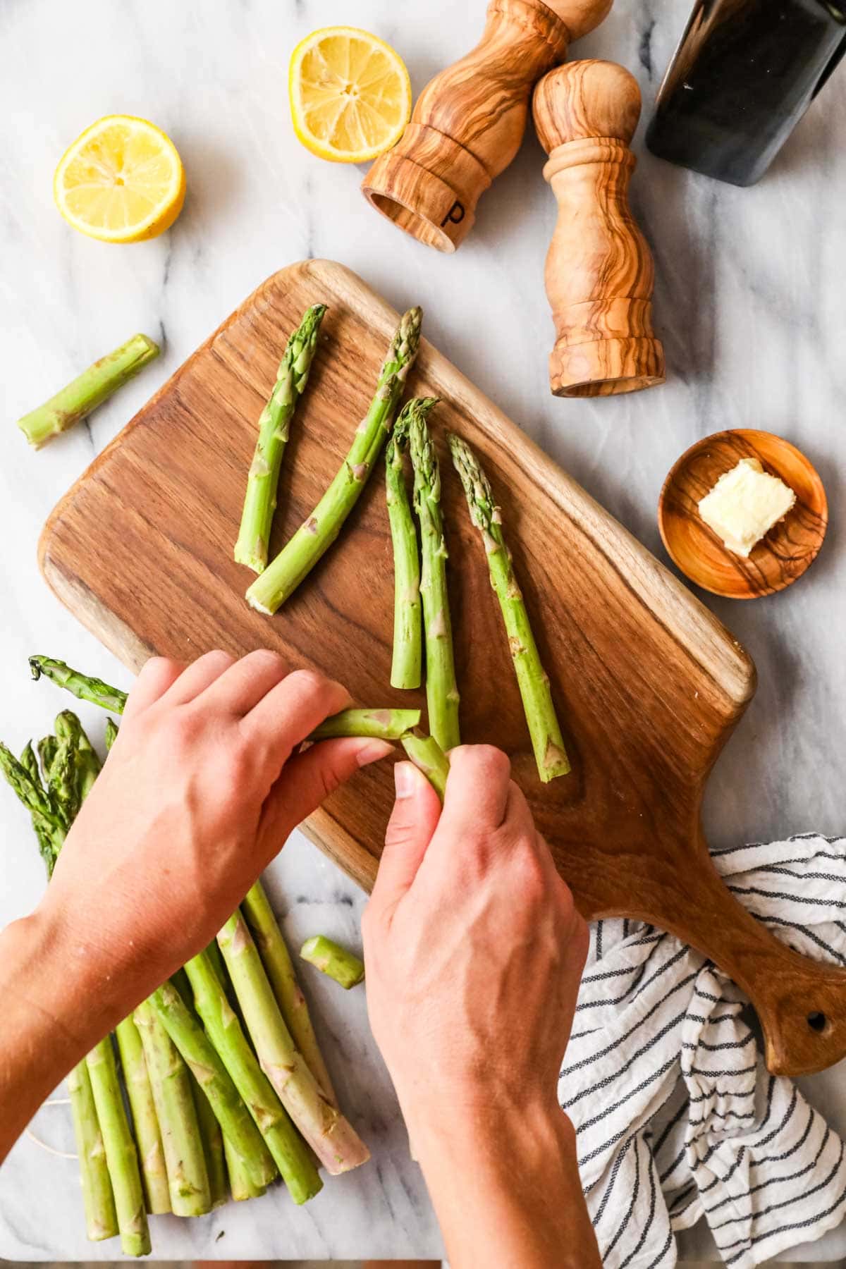 Overhead view of hands snapping woody ends off of asparagus spears.