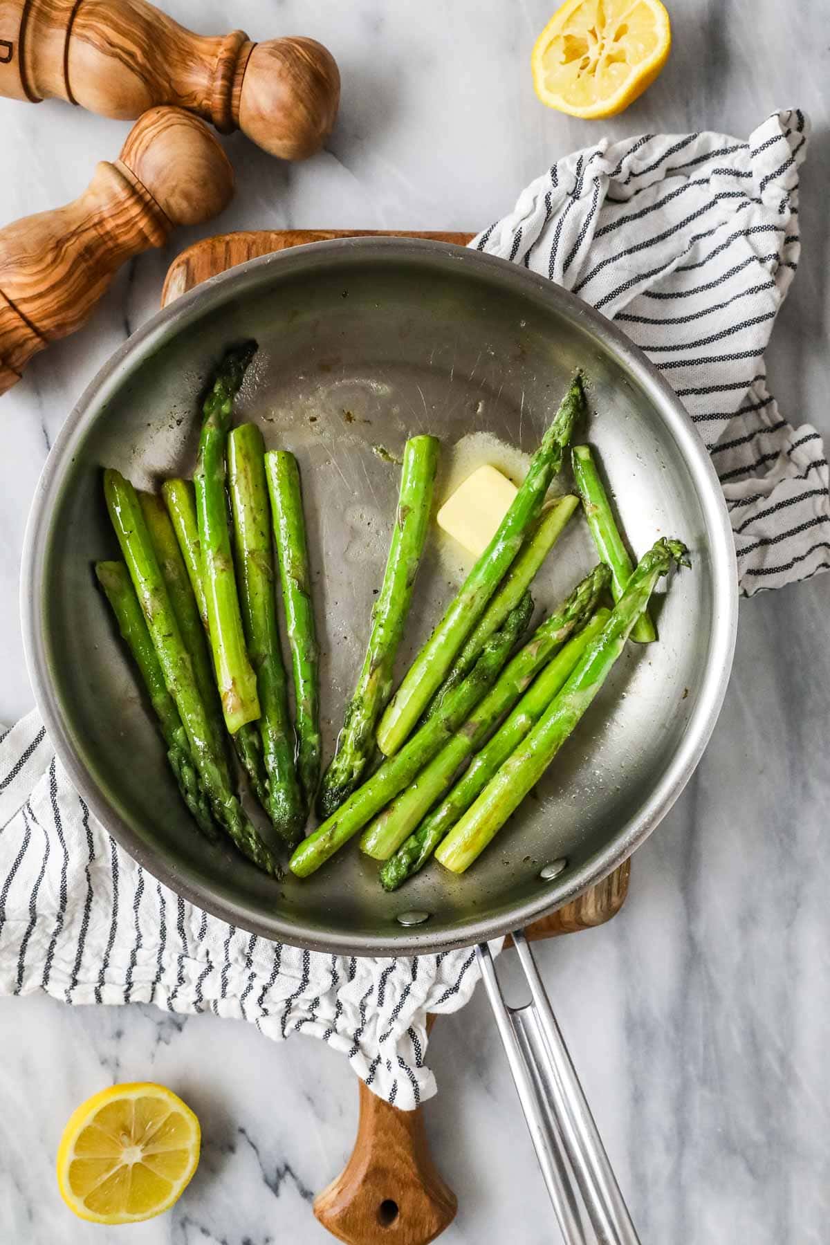 Overhead view of butter melting into a saucepan of asparagus spears.