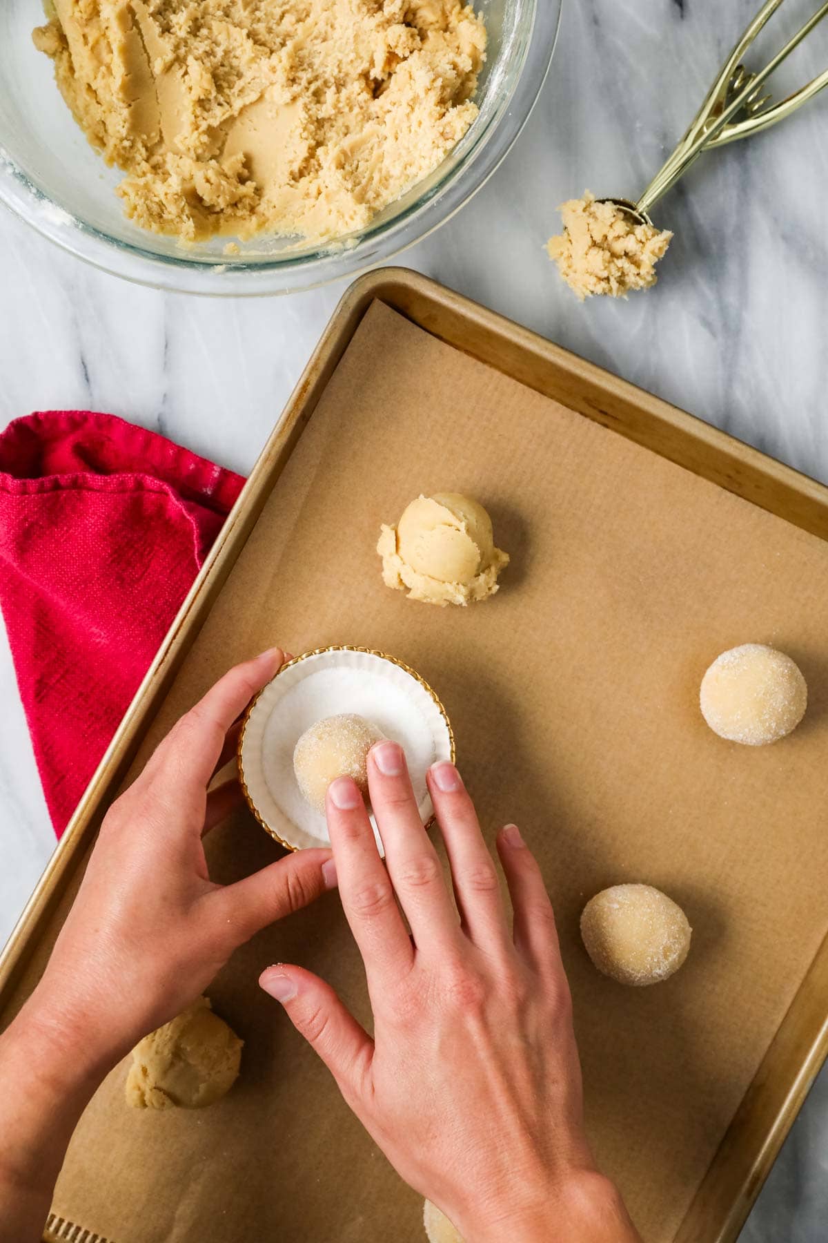 Hands rolling balls of cookie dough through granulated sugar before placing on a cookie sheet.