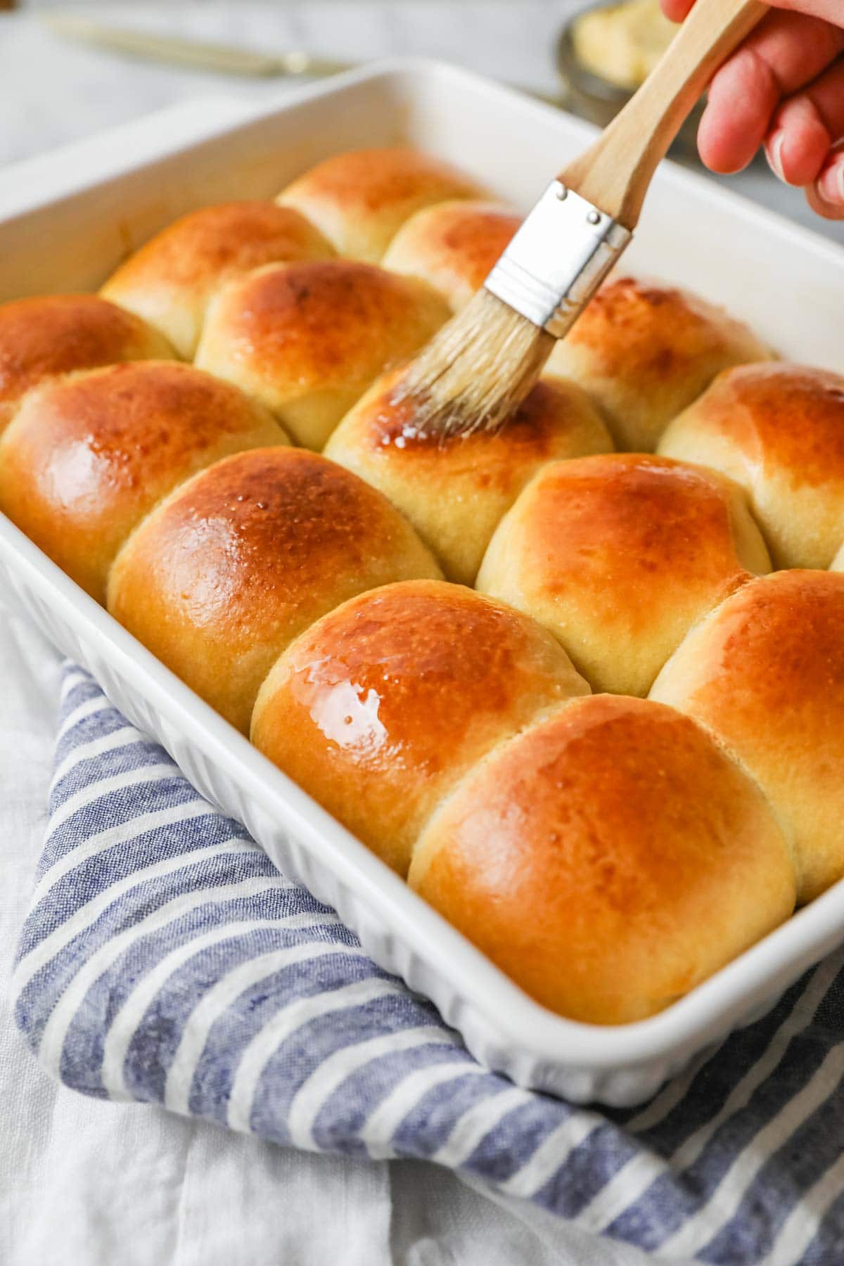 Butter being brushed on baked dinner rolls made with sourdough starter.