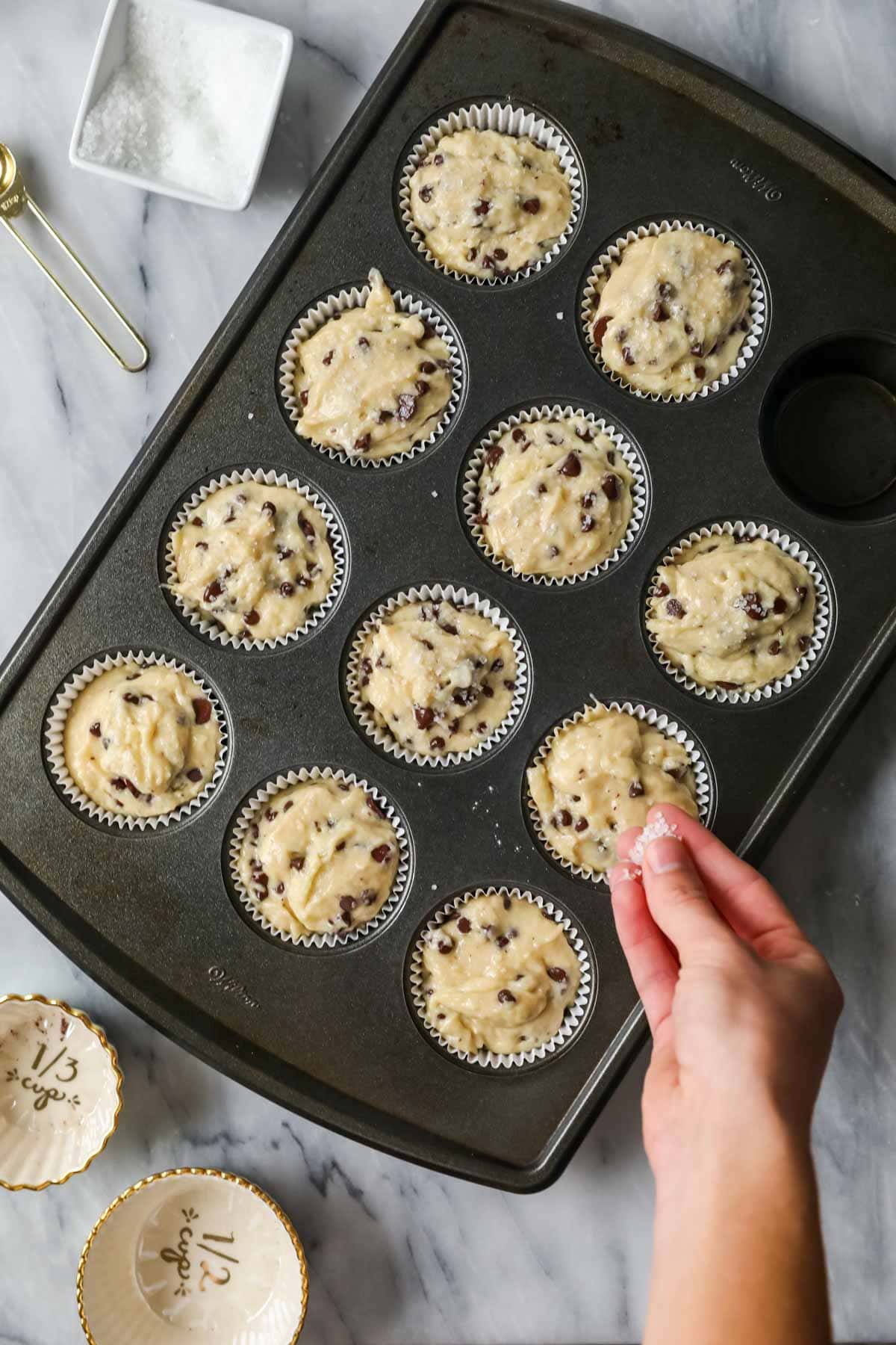 Sprinkling coarse sugar over sourdough chocolate chip muffins before baking.