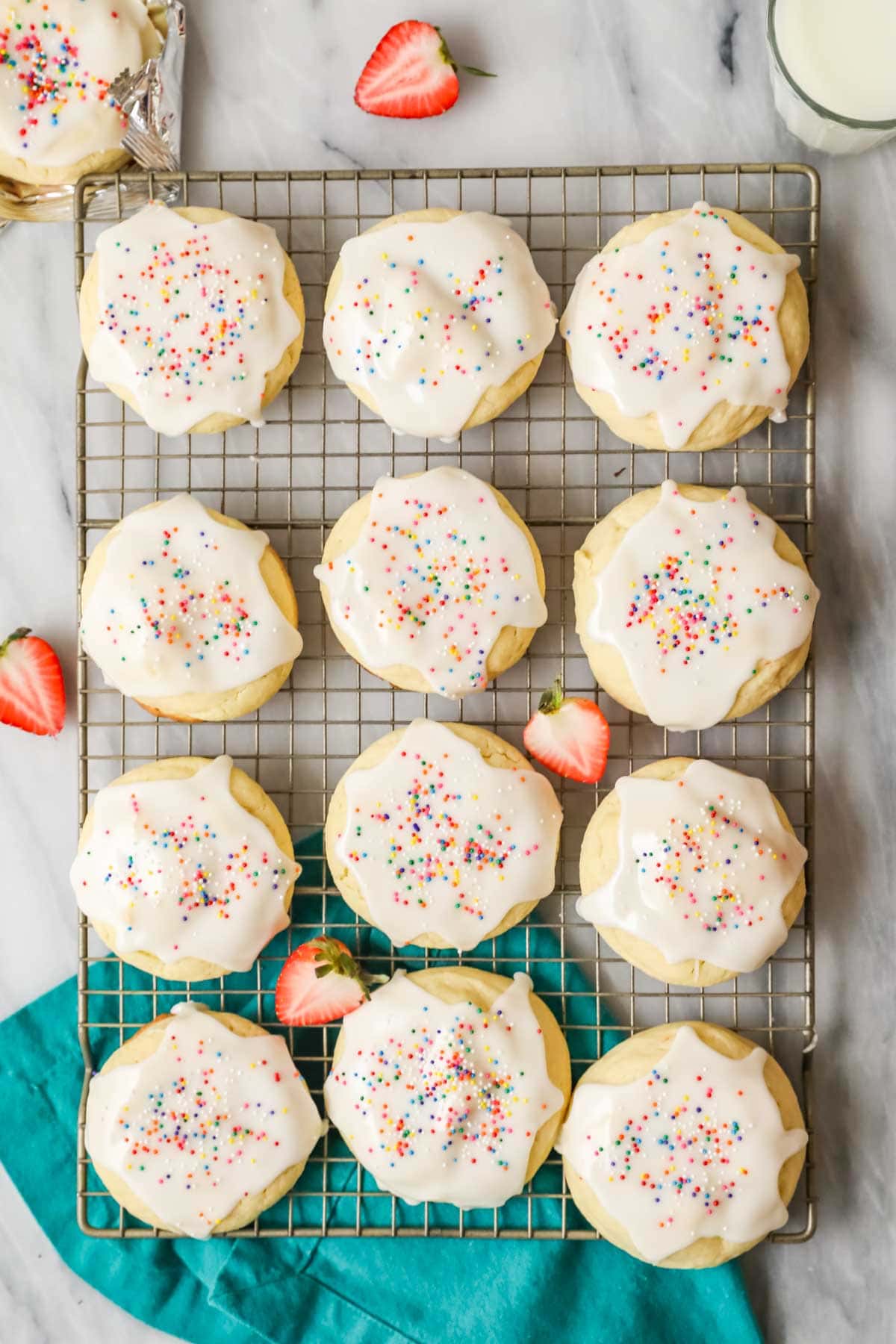 Overhead view of rows of cookies frosted with a vanilla glaze and topped with colorful nonpareil sprinkles.