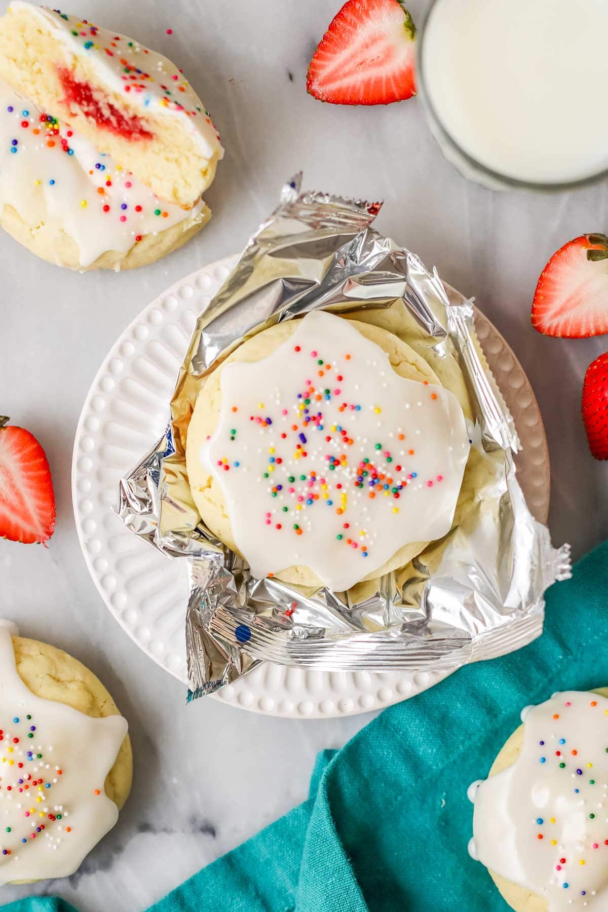 Overhead view a cookie frosted with a vanilla glaze and topped with colorful nonpareil sprinkles sitting in a foil wrapper.