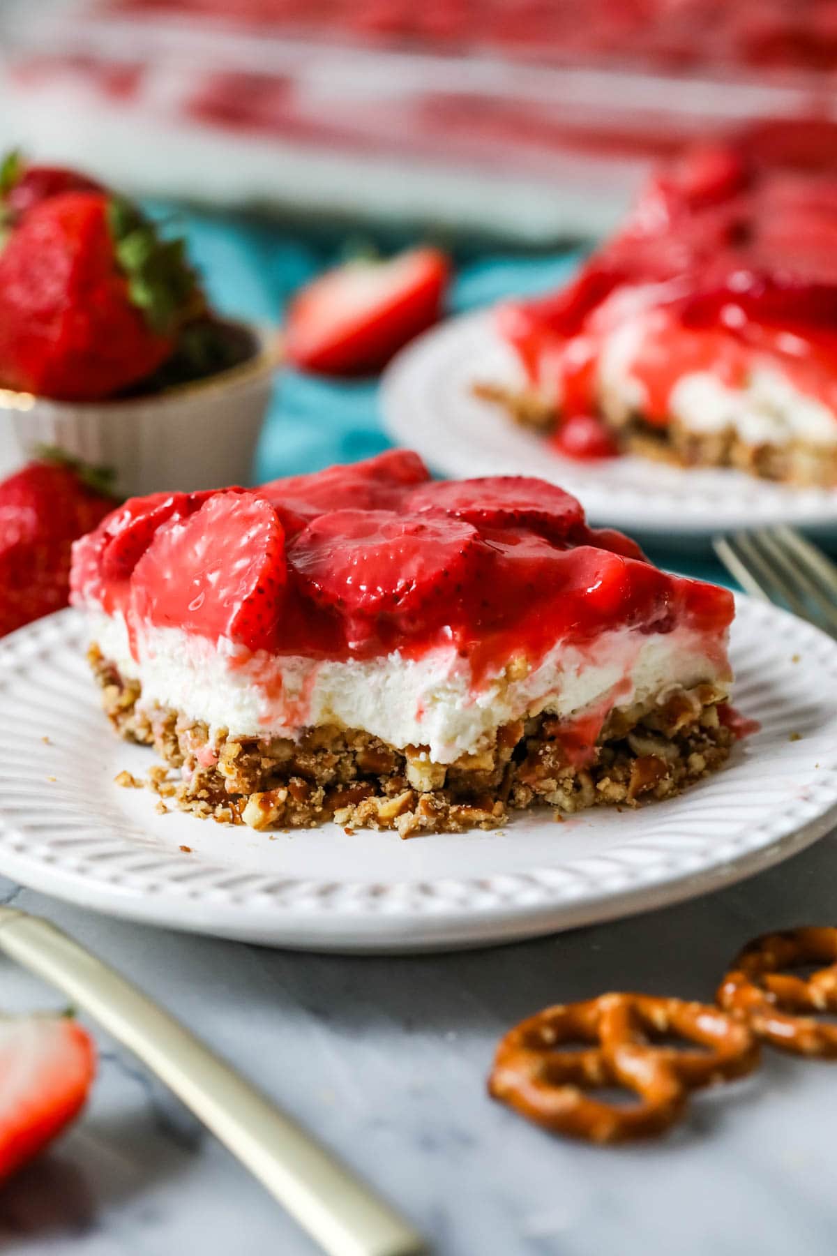 Bite missing from a layered strawberry, pretzel, and cream cheese dessert.