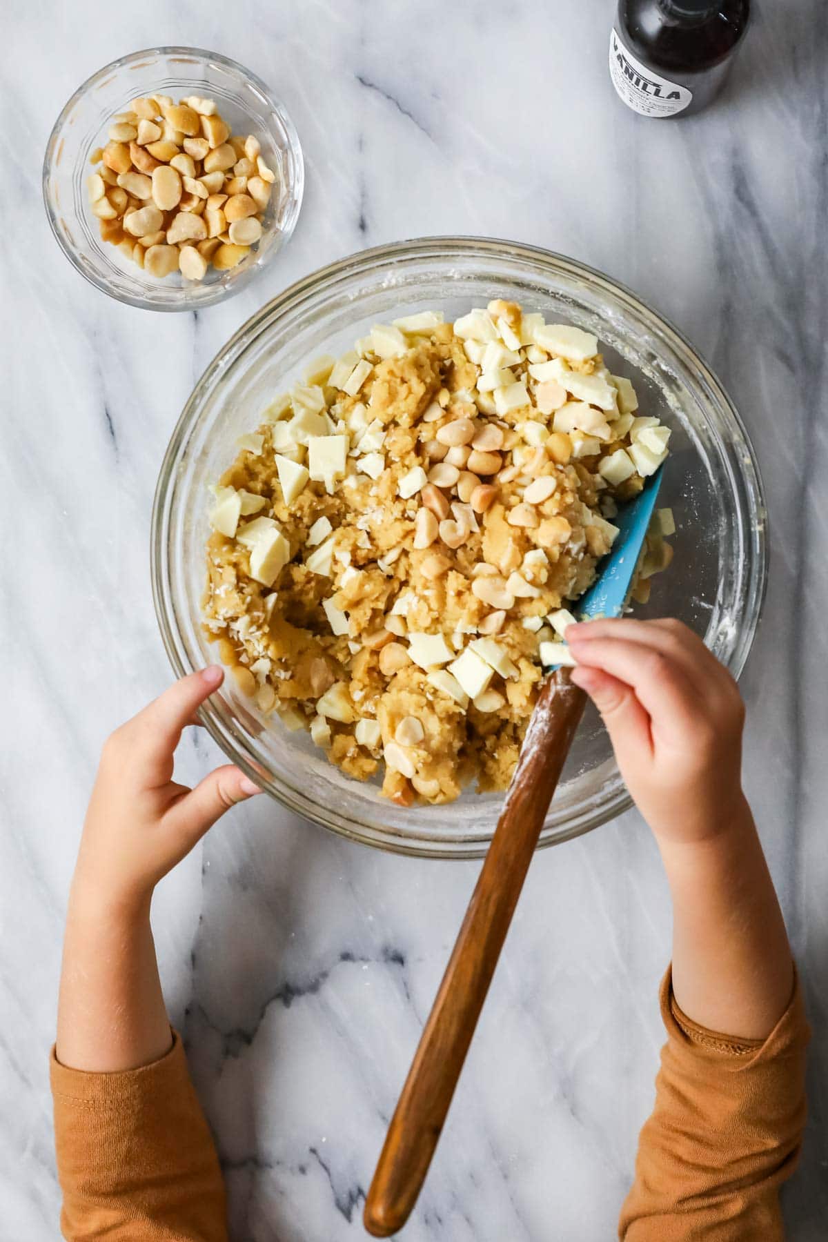 Overhead view of a bowl of cookie dough topped with white chocolate chunks and macadamia nuts.