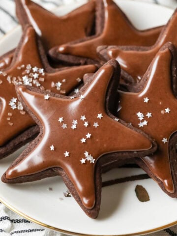 Plate of star shaped chocolate sugar cookies topped with a chocolate icing and silver star sprinkles.