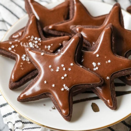 Plate of star shaped chocolate sugar cookies topped with a chocolate icing and silver star sprinkles.