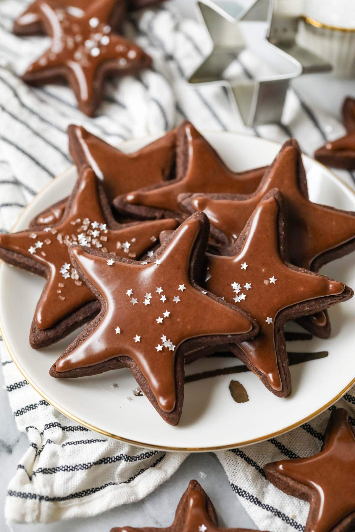 Plate of star shaped chocolate sugar cookies topped with a chocolate icing and silver star sprinkles.