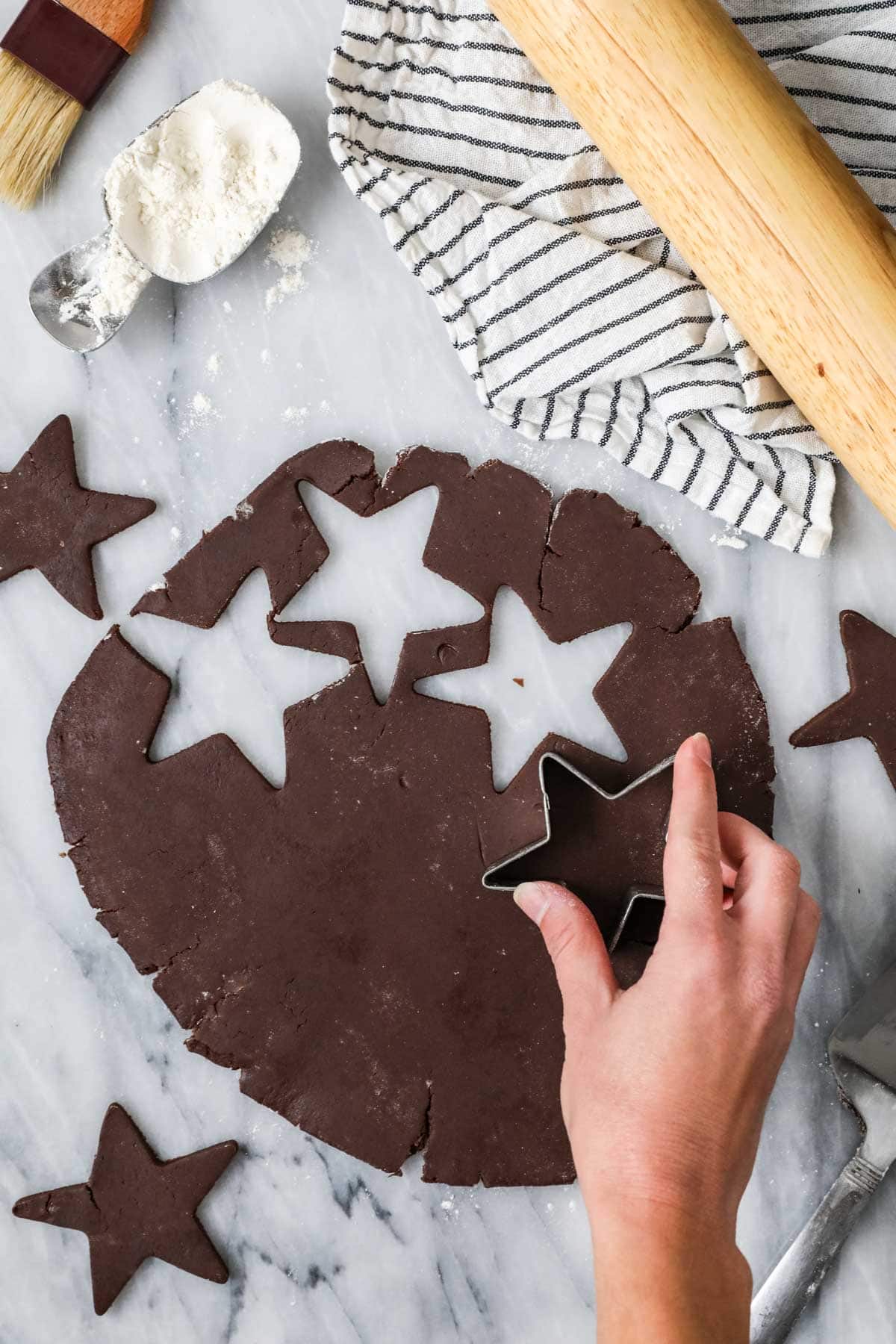 Hands cutting star cookies out of a chocolate dough.