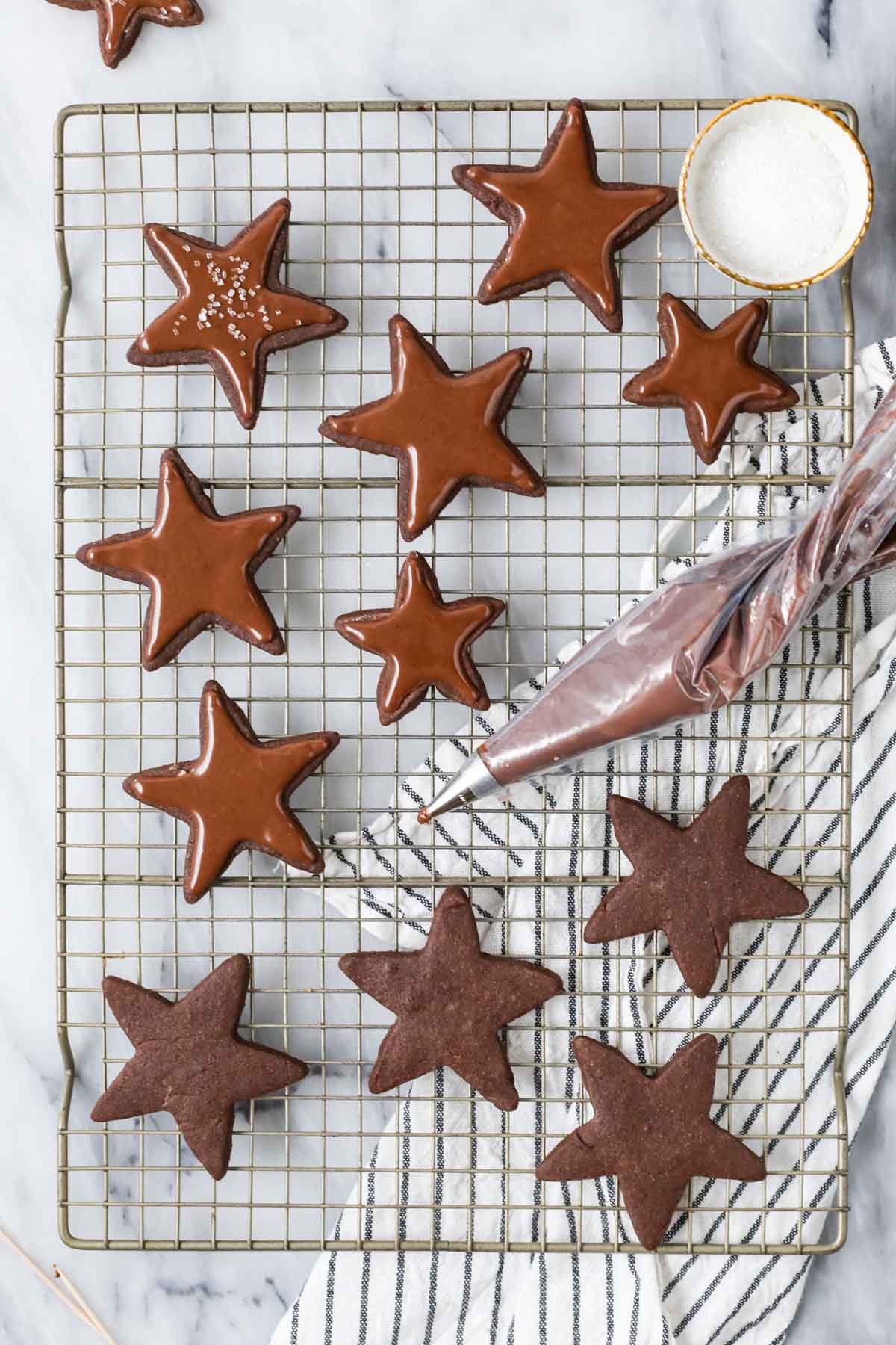 Overhead view of chocolate star cookies being topped with a piped chocolate icing.