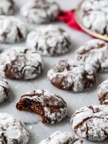 Chocolate crinkle cookies on a marble surface with a bite missing from one cookie.