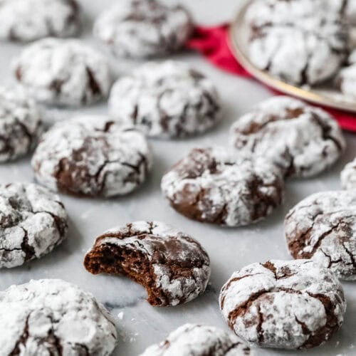 Chocolate crinkle cookies on a marble surface with a bite missing from one cookie.