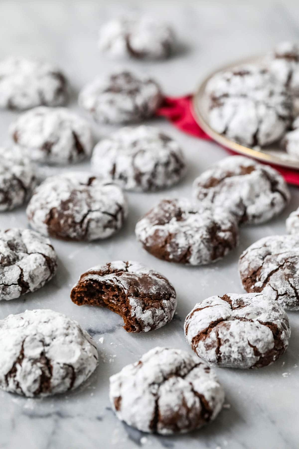 Chocolate crinkle cookies on a marble surface with a bite missing from one cookie.