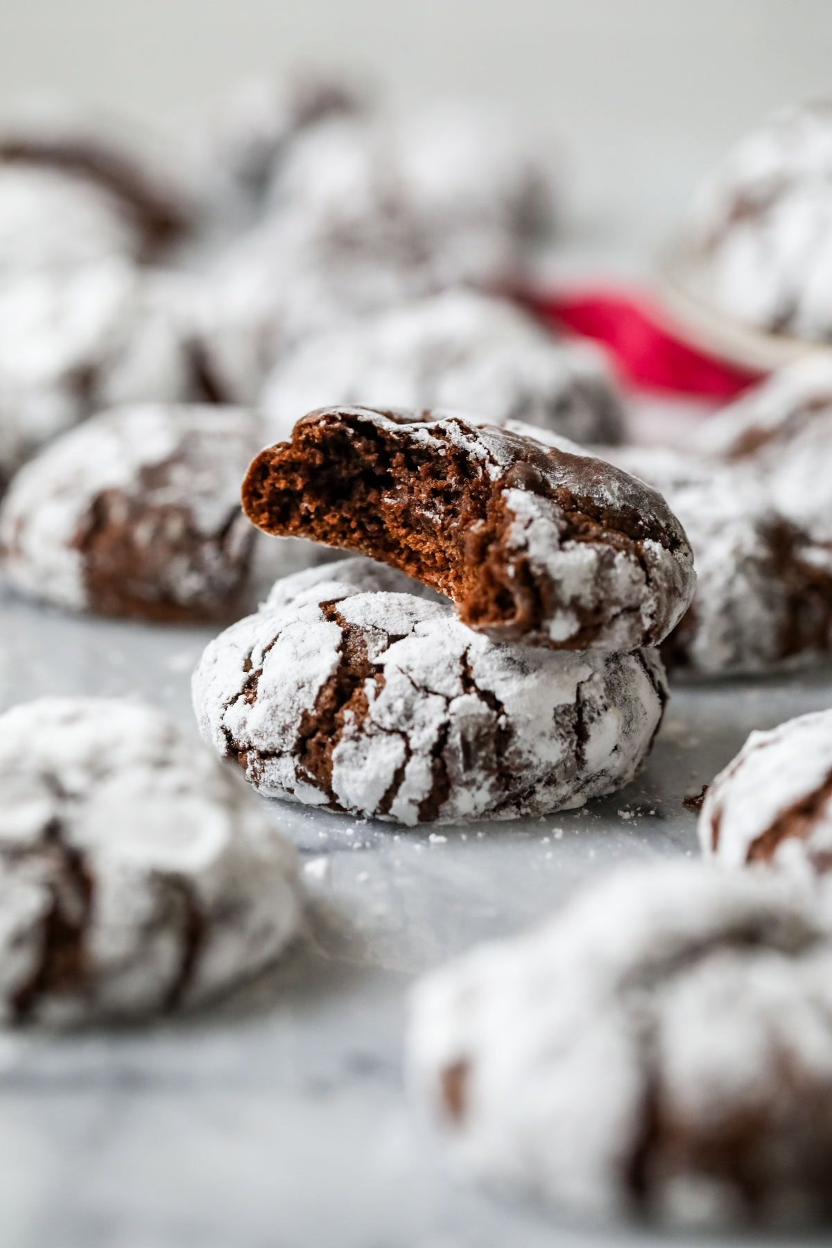 Two powdered sugar coated chocolate crinkle cookies stacked on top of each other with the top cookie missing a bite.