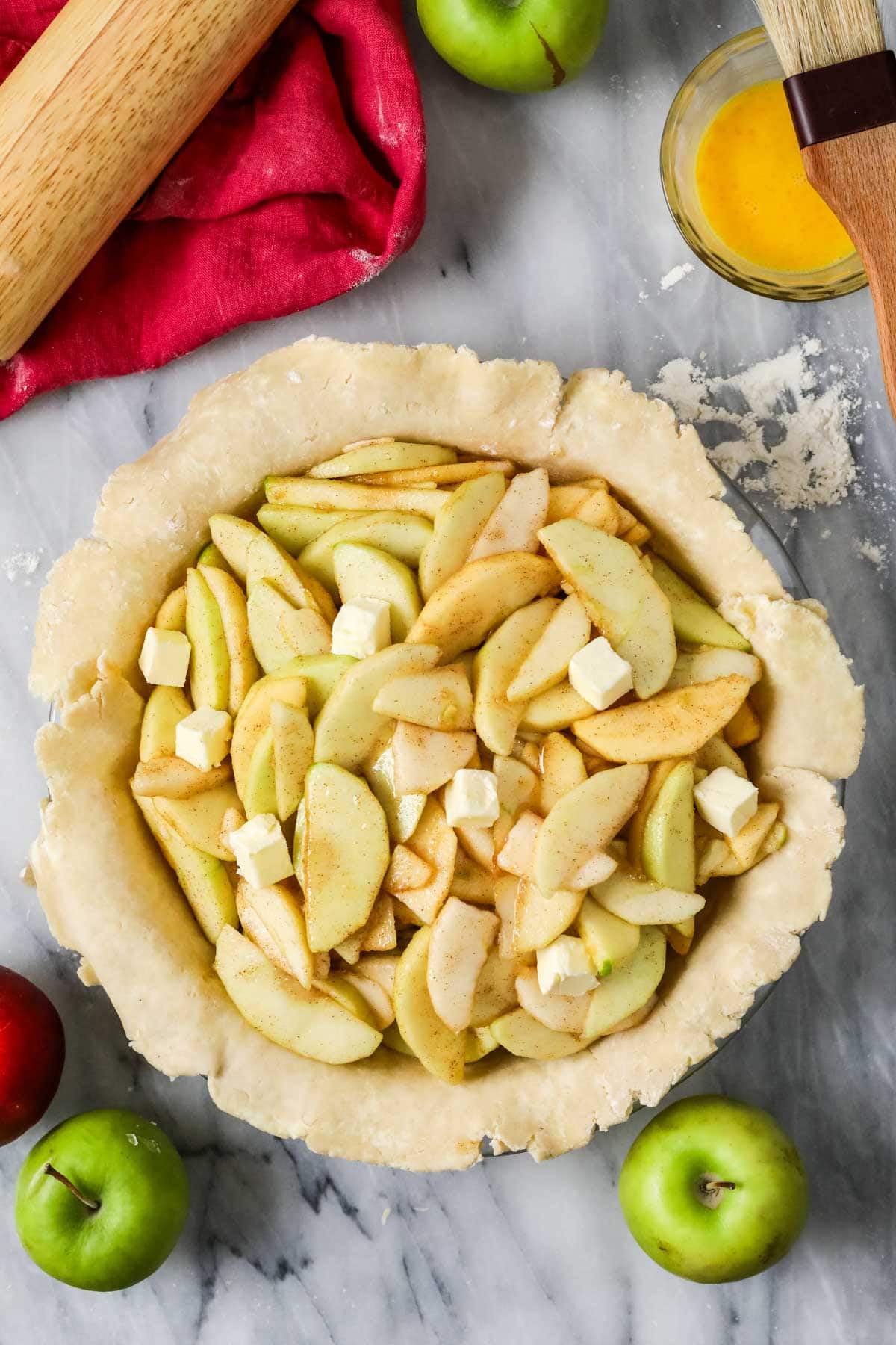 Overhead view of a pie crust filled with apples and dotted with butter pieces before adding the top crust.