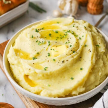 Serving bowl of garlic mashed potatoes topped with melted butter and chives.