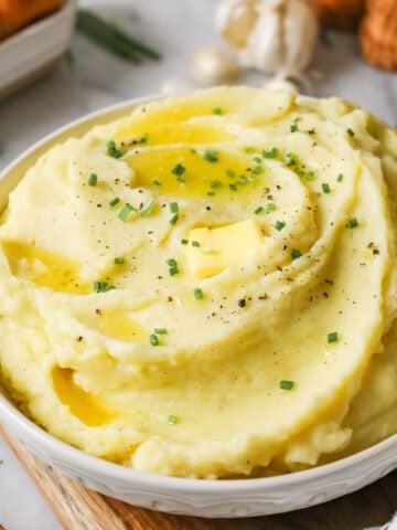 Serving bowl of garlic mashed potatoes topped with melted butter and chives.