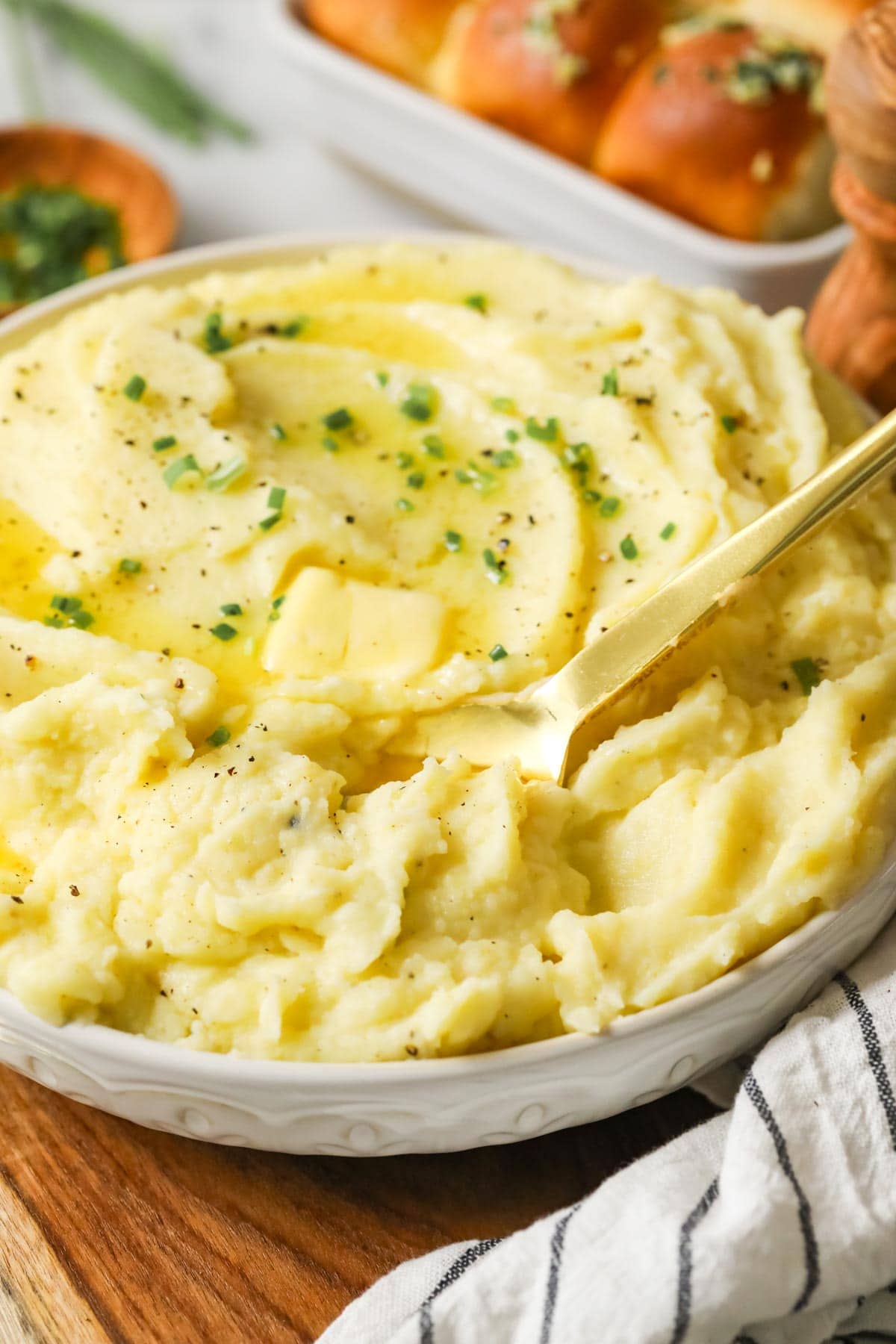 Bowl of mashed potatoes made with garlic topped with melted butter and chives.