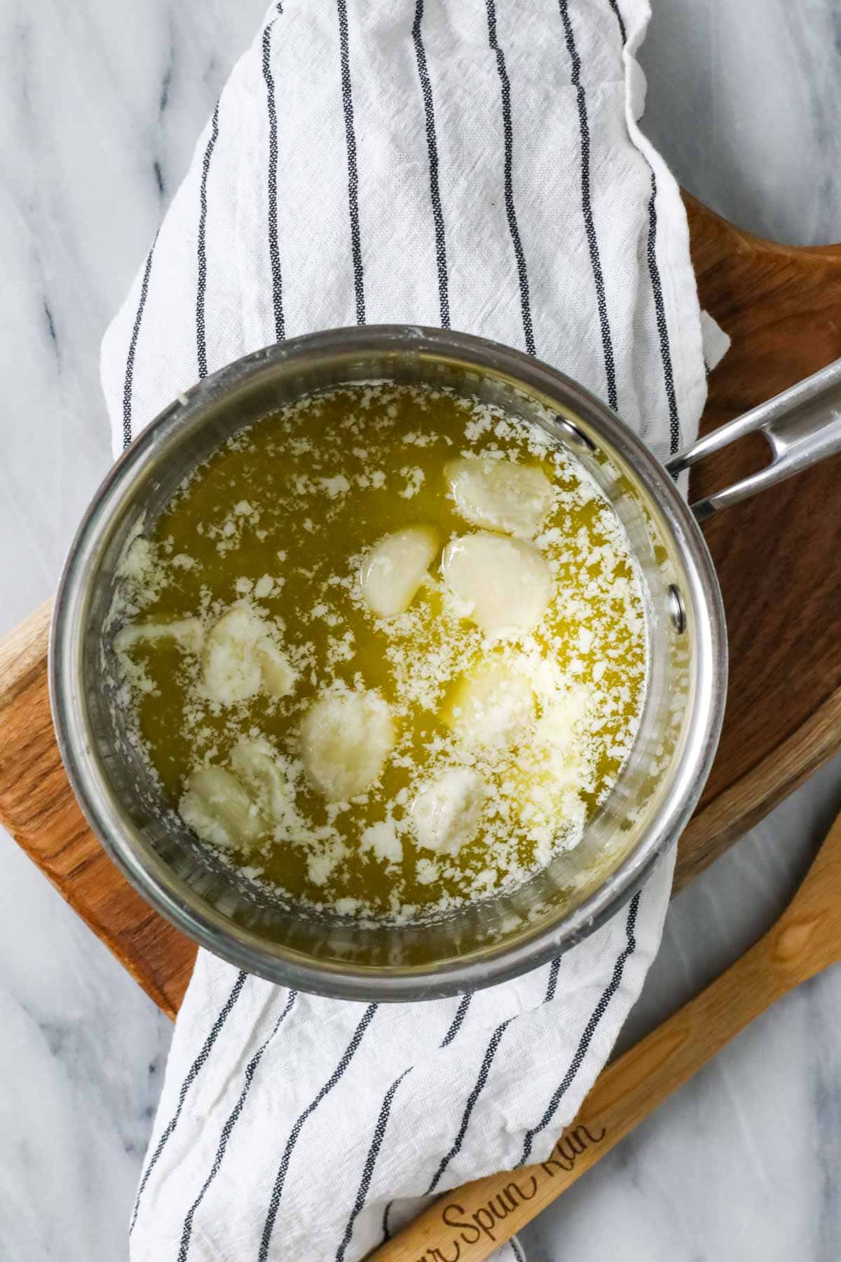 Overhead view of garlic cloves cooking in melted butter.