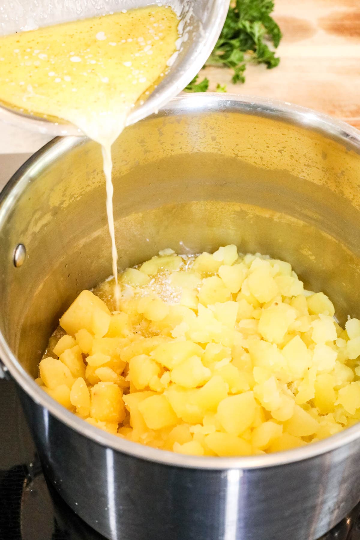 Melted butter being poured into boiled potatoes in a saucepan.