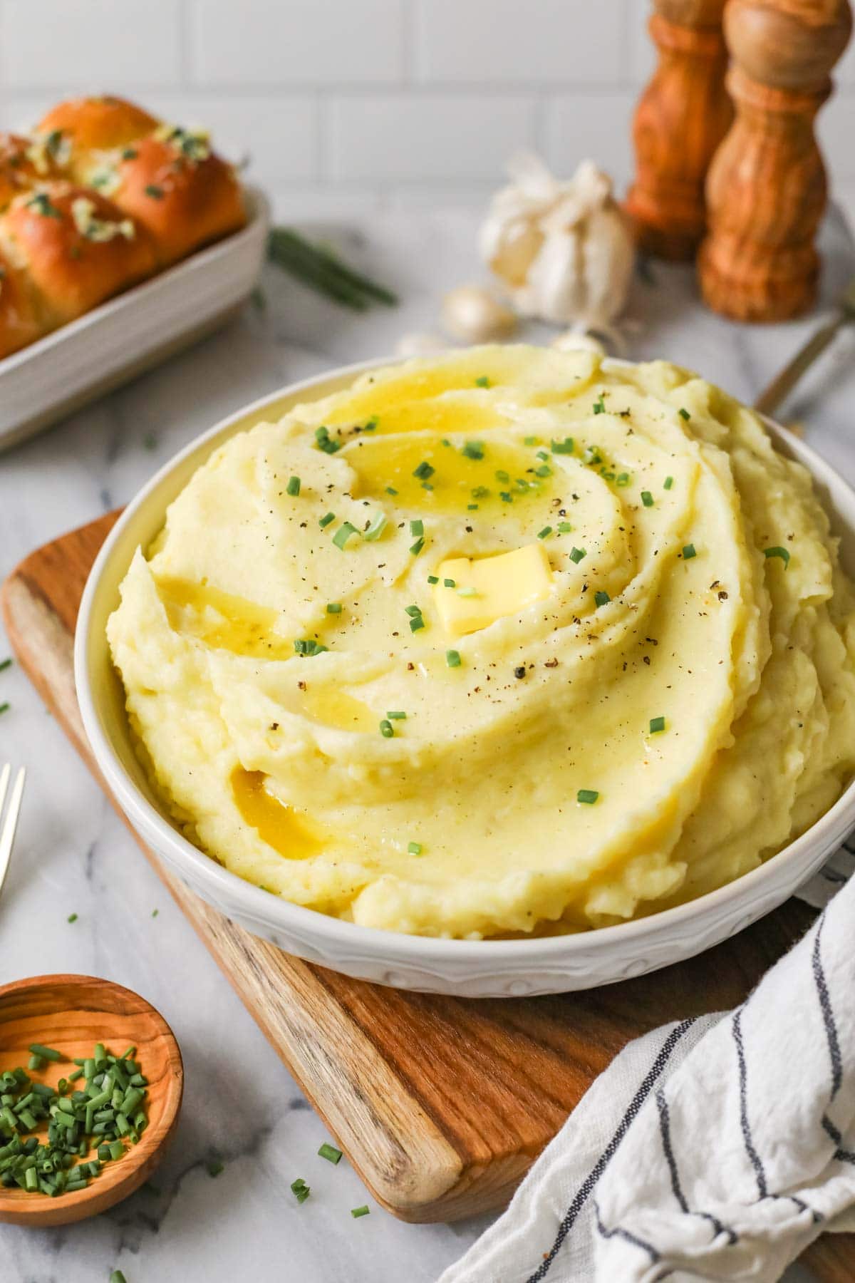 Serving bowl of garlic mashed potatoes topped with melted butter and chives.