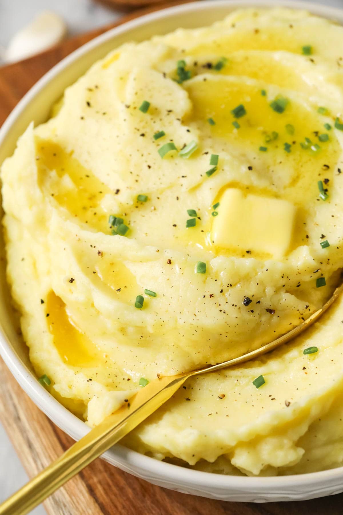 Close-up view of a butter pat melting over mashed potatoes made with garlic and chives.