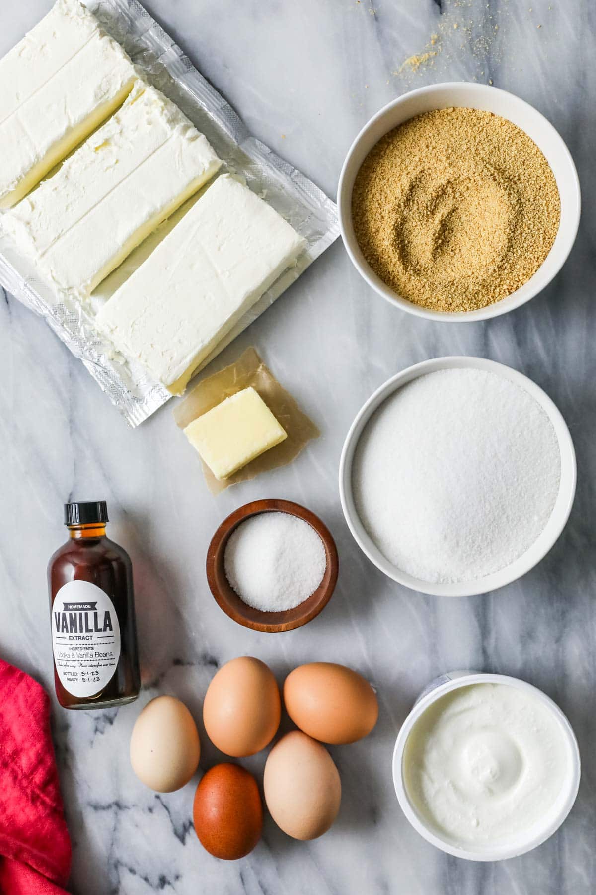 Overhead view of ingredients including graham cracker crumbs, cream cheese, sour cream, and more.