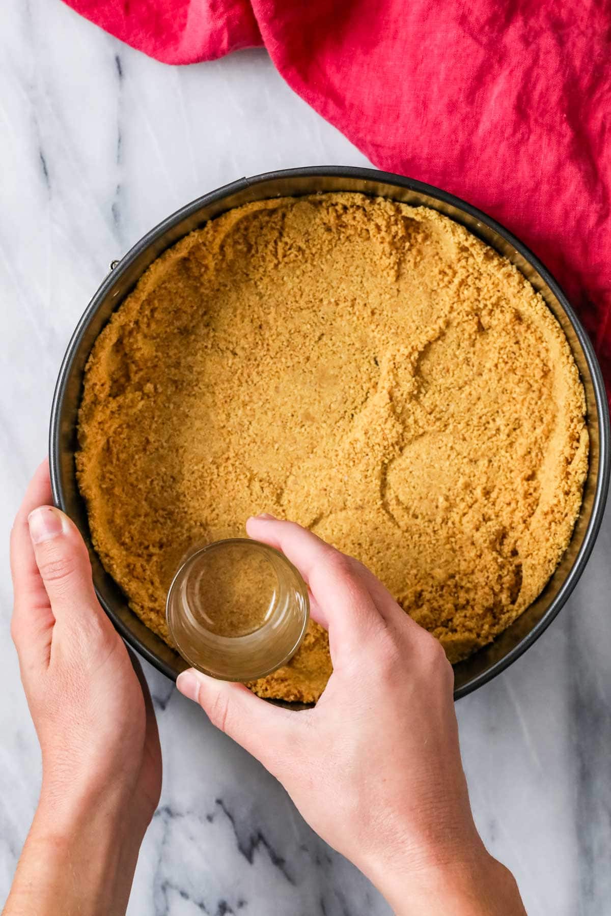 Overhead view of a graham cracker crust being pressed into the bottom of a springform pan.