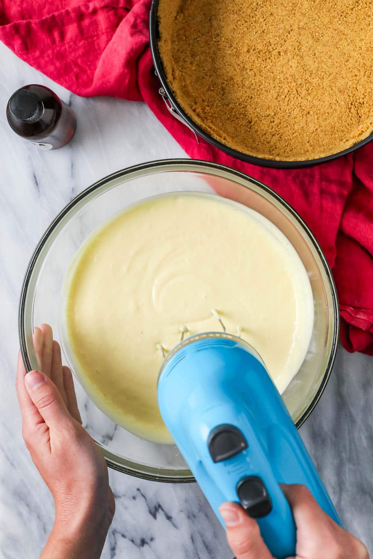 Overhead view of a mixer mixing a cheesecake batter in a bowl.