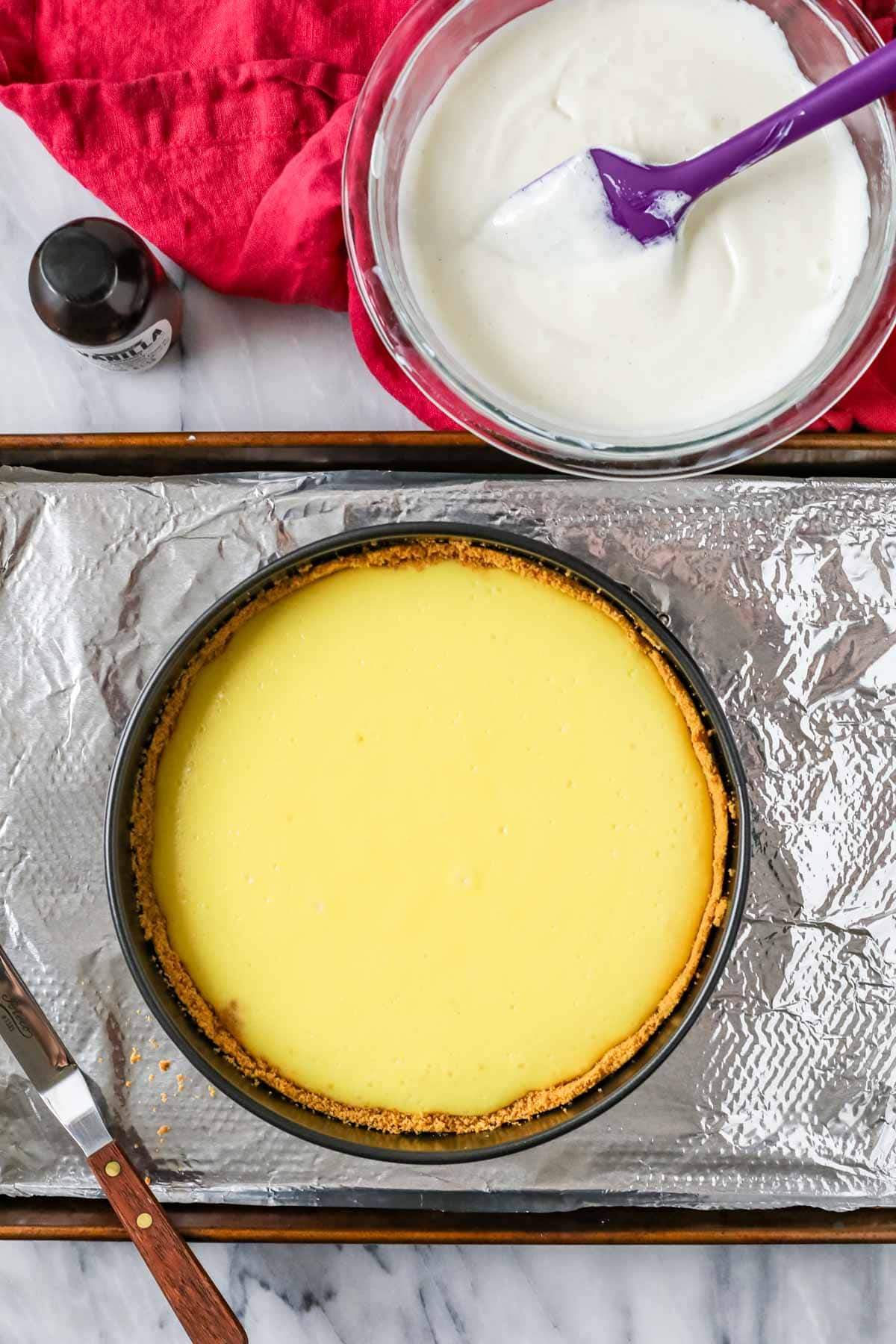 Overhead view of a baked cheesecake beside a bowl of sour cream topping.